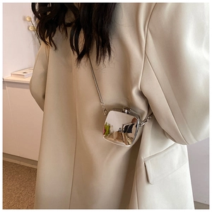 Detailed view of mini silver metal crossbody bag with chain strap on beige blazer