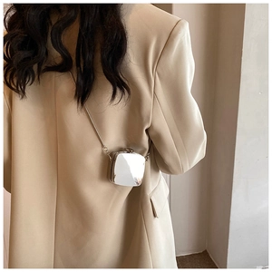 Detail of a silver mirror-finish mini box bag with a thin metal chain on a beige blazer