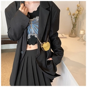 Detail of a golden mirror heart-shaped mini chain bag held by a model in fashion suit