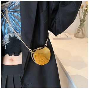 Close-up of heart-shaped gold metallic mini bag with chain on a black suit outfit