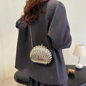 Silver metallic shell-shaped crossbody bag with chain strap on grey blazer model