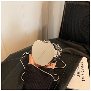 Detail of silver heart-shaped mirror clutch bag with metallic chain on black leather