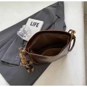 Brown leather bucket bag with striped lining and cute plush bunny charm on dark blazer