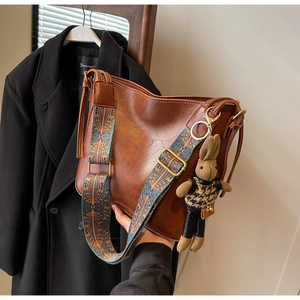 Vintage brown bucket bag with patterned strap and cute rabbit pendant shown in hand