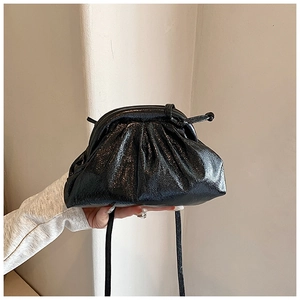 Detail of black pleated cloud bag in glossy leather held by hand against a white wall
