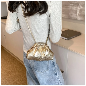Back view of model wearing a metallic gold pleated dumpling bag with cross-body strap