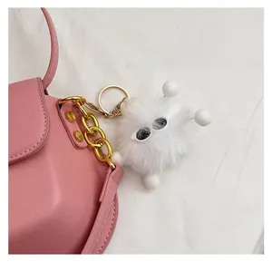 Dettaglio di un ciondolo pompon di pelliccia sintetica bianca con occhiali su borsa rosa