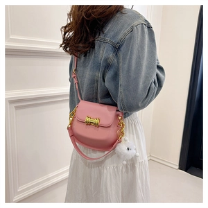Borsa a sella rosa con fibbia dorata, catena e ciondolo di peluche su outfit in denim blu