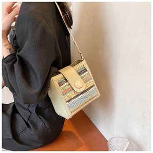 Detail of multi-color woven straw crossbody bag with green leather trim and round buckle