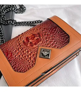 Detail view of orange and brown snakeskin crossbody bag with black metal chain and clasp