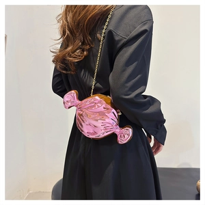 Pink metallic candy shaped crossbody bag with gold chain strap on black outfit