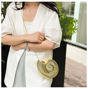 Detail of golden nautilus shell evening bag with metallic chain on white outfit