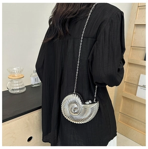 Detail of nautilus shaped silver evening bag with metallic chain on model