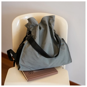 Detail of grey canvas tote bag with black leather strap and textured folds on chair