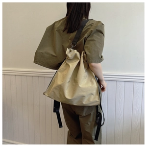 Detail of canvas bag showing durable beige fabric and black nylon strap on model
