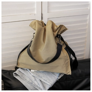 Detail of a khaki canvas bucket bag with a black wide strap on a white background
