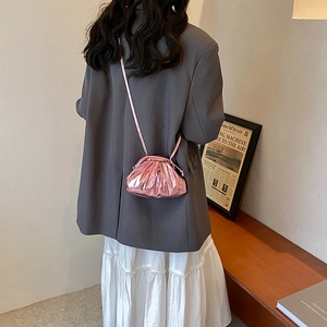 Metallic pink pleated cloud bag with slim shoulder strap worn by a model in lifestyle setting