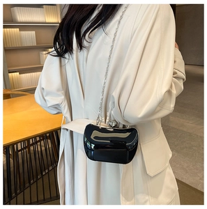 Detail of a black glossy evening clutch with silver heart buckle and chain on a person