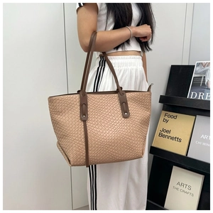 Dettaglio della borsa tote intrecciata kaki con manici marroni indossata a spalla
