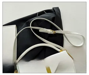 Detail showing white minimalist saddle bag with gold metal lock and adjustable shoulder strap