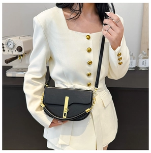 Model wearing black saddle bag with gold hardware and chain strap on tweed jacket