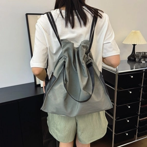 Minimalist sage green drawstring shoulder bag worn by model in a modern home setting