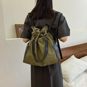 Olive green drawstring backpack with black leather straps shown on a person's back