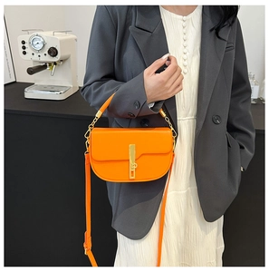 Detail showing bright orange saddle bag with gold metal buckle and leather strap on a model
