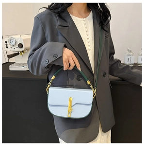 Light blue saddle bag with dark green handles and gold hardware shown in lifestyle scene