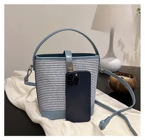 Confronto delle dimensioni della borsa a secchiello in paglia accanto a uno smartphone blu