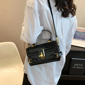 Sac à main français en cuir verni noir avec fermoir doré porté en bandoulière chic