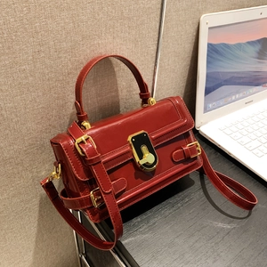 Sac à main bandoulière vintage en cuir brillant bordeaux avec boucle dorée sur bureau