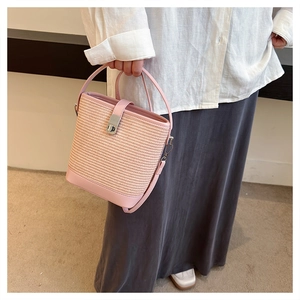 Dettaglio borsa a secchiello in paglia intrecciata rosa con finiture in pelle e chiusura a vite