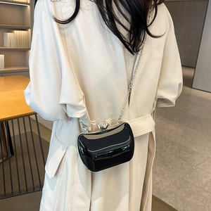 Minimalist black patent leather evening bag with silver chain strap worn by a model