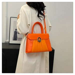 Détail du sac à main orange plissé en cuir avec boucle en métal porté sur un trench blanc