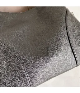 Close-up of litchi grain leather texture and fine stitching on a minimalist crossbody bag