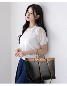 Close-up of black textured tote bag with brown leather handles and gold metal hardware