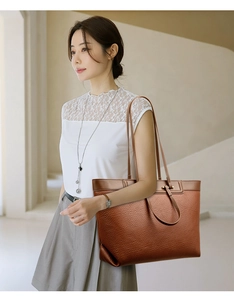 Close-up of brown pebbled leather tote bag with fine stitching on a shoulder strap