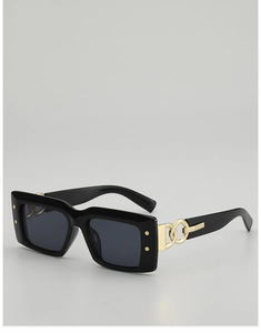 Détail de lunettes de soleil noires rectangulaires avec branches chaînées dorées et rivets