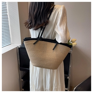 Détail d'un grand sac cabas en paille avec bordure noire porté à l'épaule par un mannequin