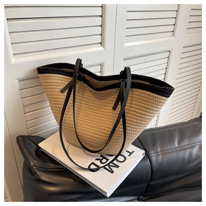 Détail d'un sac cabas en paille avec bandoulière noire sur un canapé en cuir