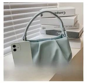 Close-up of light blue pleated handbag with smartphone for size comparison