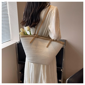 Sac fourre-tout tissé minimaliste avec bordure brune porté par un mannequin pour la plage