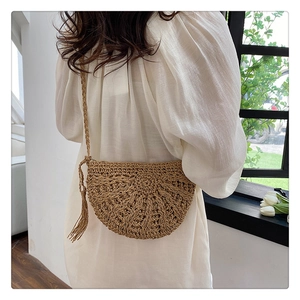 Detail view of woven straw crossbody bag with tassel and textured half-moon design