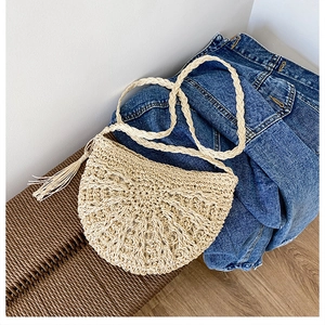 Detail of handmade crochet straw crossbody bag with fringe tassel on denim background