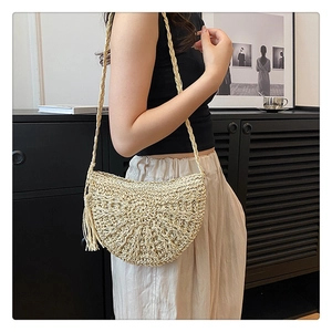 Detail of beige half-moon straw bag with woven strap and decorative tassel charm