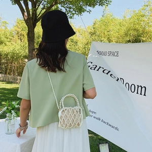Elegant off-white beaded bucket bag with pearl strap and interior pouch in a garden setting