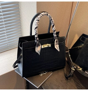 Detail of black crocodile texture leather handbag with silk scarf and gold clasp