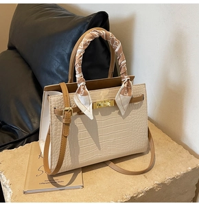 Detail of cream croc-embossed handbag featuring gold twist lock and silk scarf handle decor