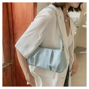 Chic light blue pleated cloud bag worn by model over a white blazer in a cozy setting